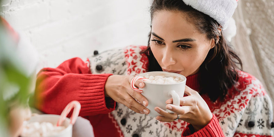 two women in Christmas winter outfit holding a white cup of hot cocoa