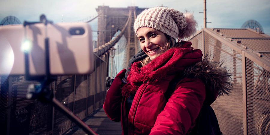 woman in red zip-up hooded winter jacket holding a selfie stick with a smartphone
